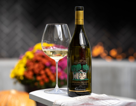 A bottle and a glass of Frank Family's Carneros Chardonnay in front of colorful flowers and a fireplace. 
