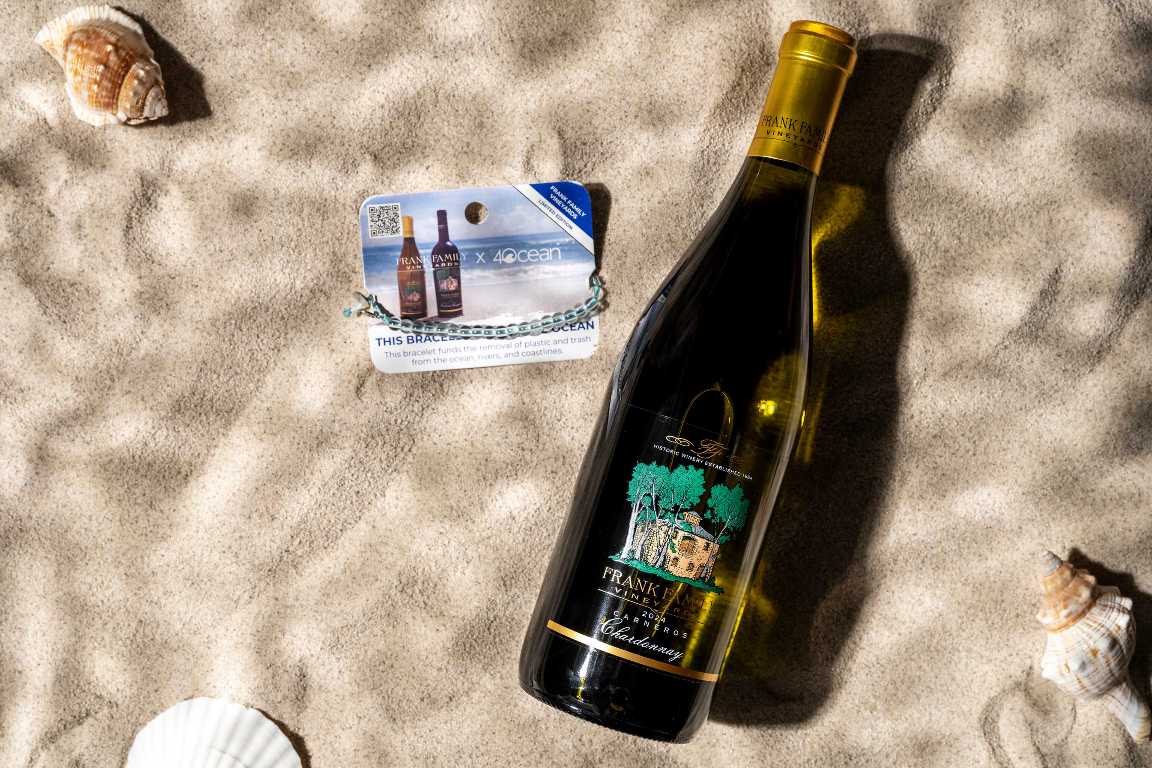 A bottle of Carneros Chardonnay on the beach alongside a blue 4ocean x Frank Family custom bracelet.