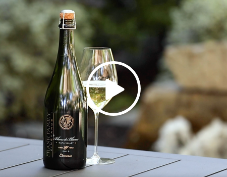 A bottle od Blanc de Blancs in a park-like setting with a fountain. 